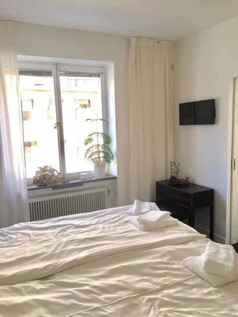 Ljust vardagsrum med soffa och konst i lägenhet på Södermalm; Stort sovrum med dubbelsäng på Södermalm; Enkelt sovrum på Södermalm; Ytterligare enkelt sovrum på Södermalm; Utrustat kök med spis och kyl på Södermalm; Privat terrass på lugn gata i Södermalm